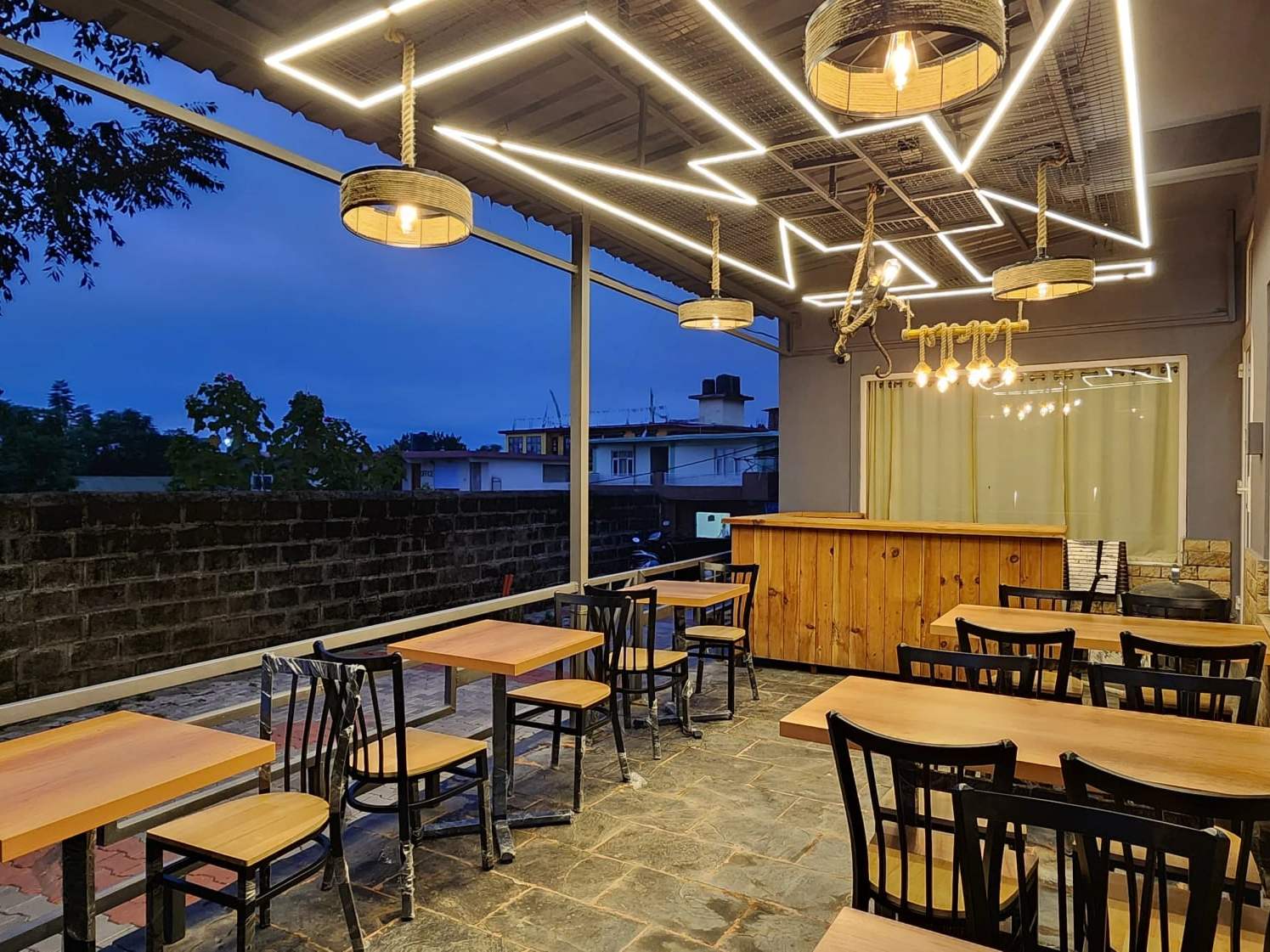 The open-air restaurant terrace at dusk, under a ceiling of zig-zag light strips