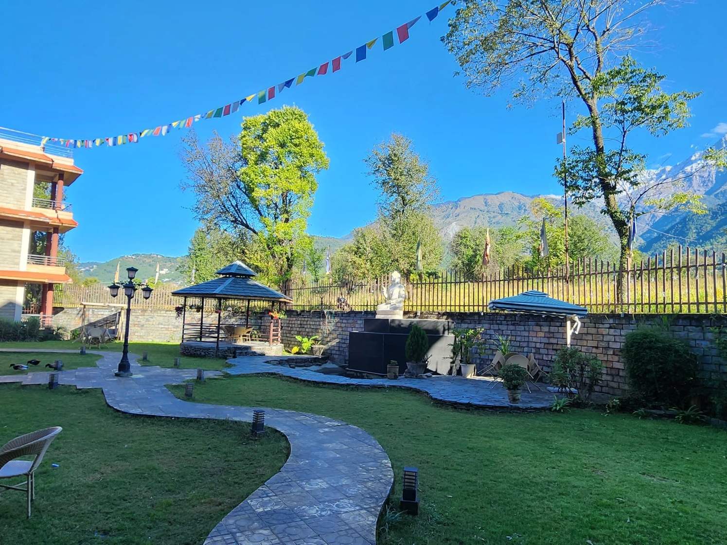 A garden with a gazebo, lawns and prayer flags under a blue sky in Dharamshala