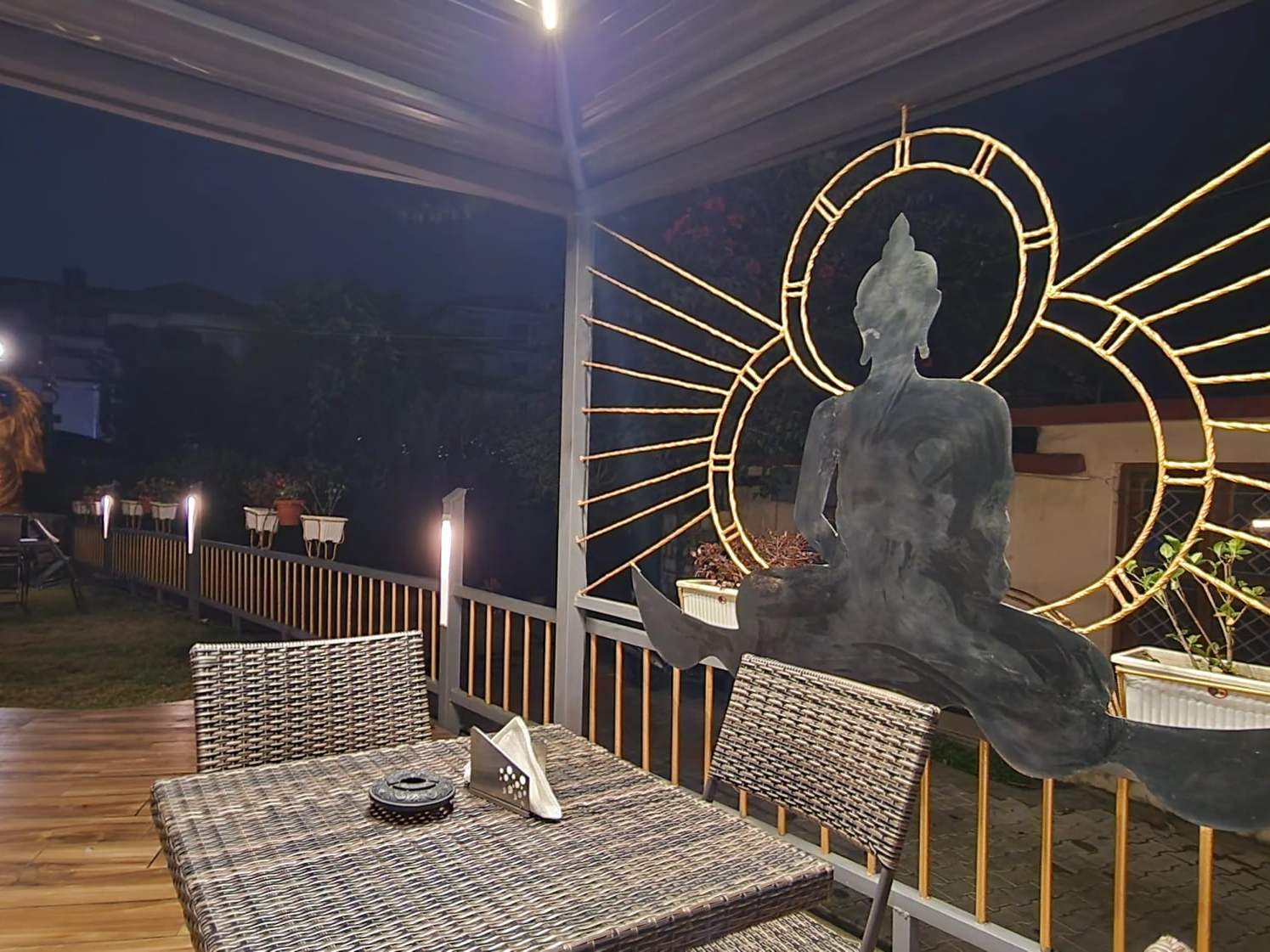 A terrace table beside a seated Buddha sculpture in a golden halo