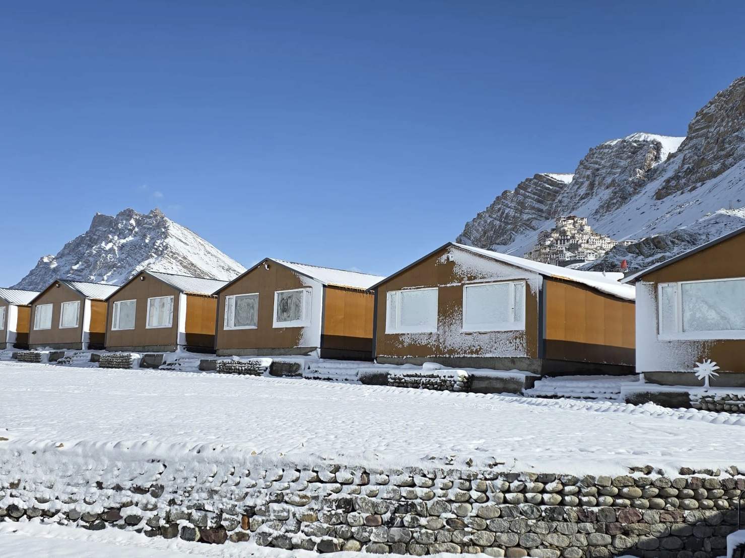 Hotel Spiti Villa’s row of wooden cottages in fresh snow, below the mountains of Spiti