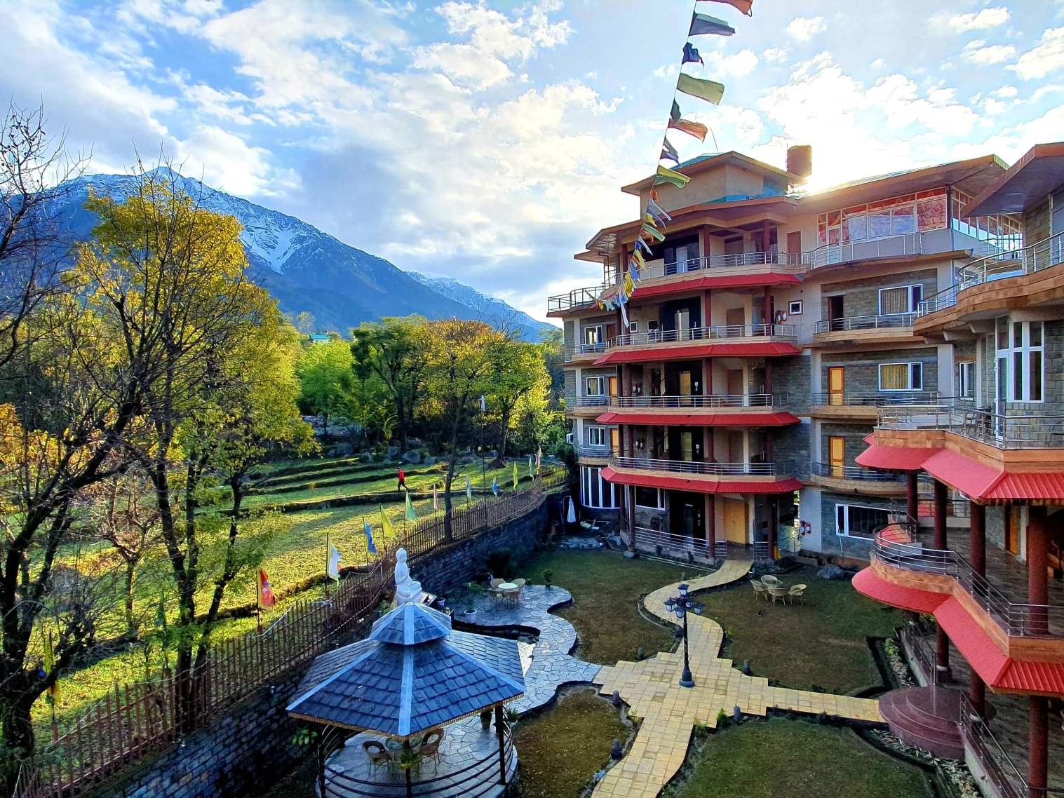 Quartz Himalayan Brothers: a multi-storey hotel with red balconies and a landscaped garden below snow-capped mountains