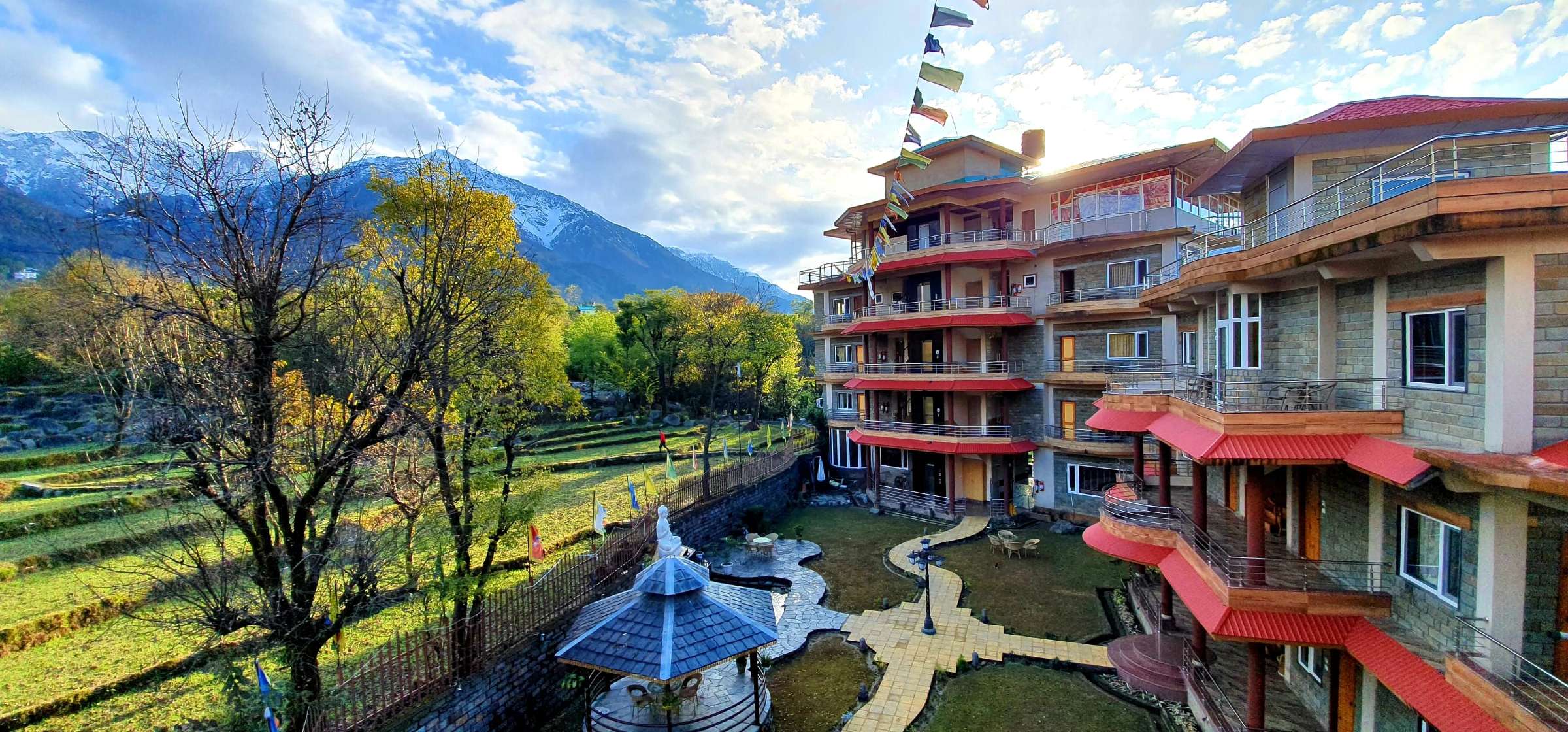 Quartz Himalayan Brothers: a multi-storey hotel with red balconies and a landscaped garden below snow-capped mountains