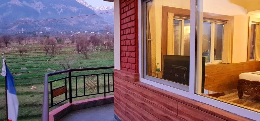A Samdupling room’s private balcony looking across green fields to the Dhauladhar mountains