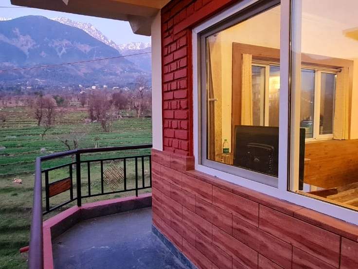 A Samdupling room’s private balcony looking across green fields to the Dhauladhar mountains